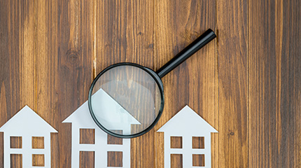 paper cutouts of homes on a wooden table with a magnifying glass