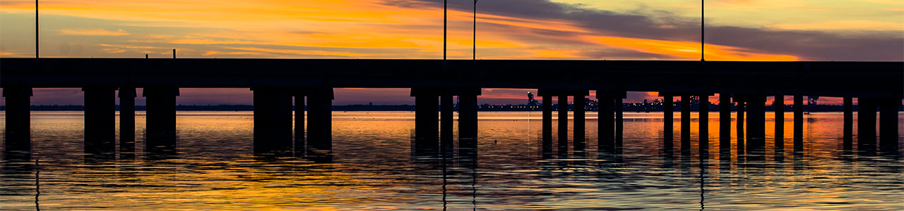 A low bridge stands in front of a Gulf Coast sunset.