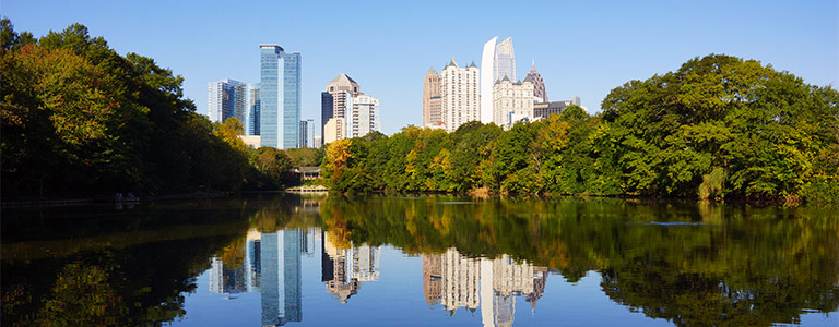 The skyscrapers of downtown Atlanta in front of the forested shore of Piedmont Park.