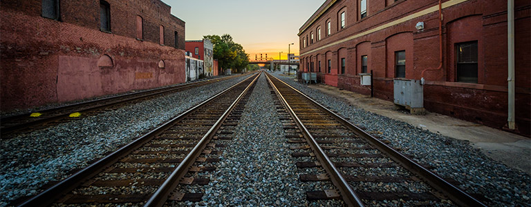 Three railroad tracks stretch into the distance along city blocks.